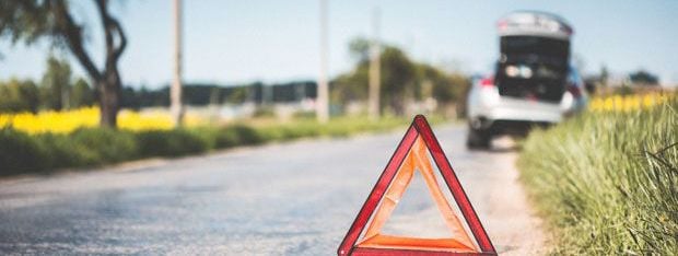 A car parked half on the road and half on the grass with its boot open and a red warning triangle behind it