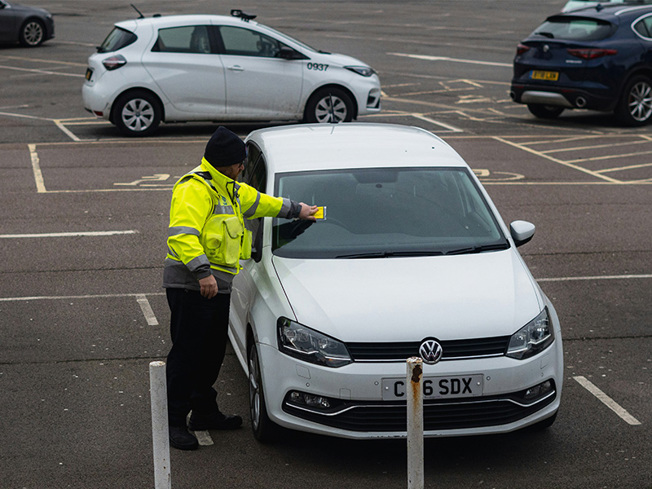 Parking officer issuing a ticket to a white Volkswagen Polo in a UK car park