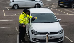 Parking officer issuing a ticket to a white Volkswagen Polo in a UK car park