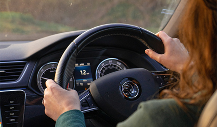 Image captured from over a woman’s shoulder in a car, showing her hands on the steering wheel