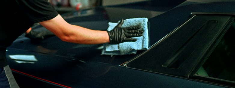 a person polishing a dark blue car with cloth