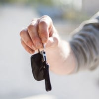 Close-up of a hand handing over car keys, signifying purchase or rental.