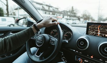 Person driving an Audi with one hand on the steering wheel