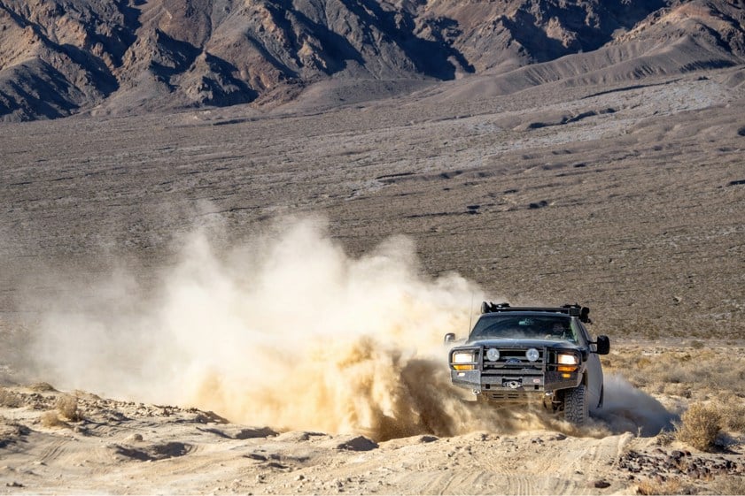 Black SUV driving off-road on sand with dust in the air