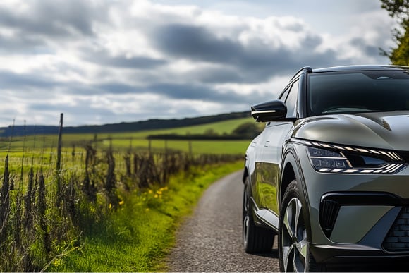 Close-up of a modern SUV parked on a rural road with green fields and cloudy skies in the background