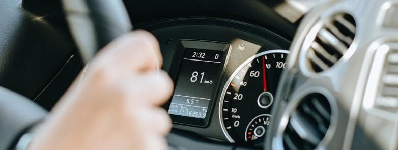 Driver with a hand on the wheel and the cars digital instrument display in the rear