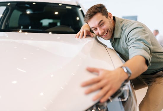 Portrait of happy smiling customer male hugging, stroking car hood after purchased in dealership, closeup