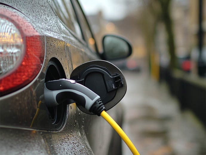 Grey electric car parked on the side of the road plugged into charge