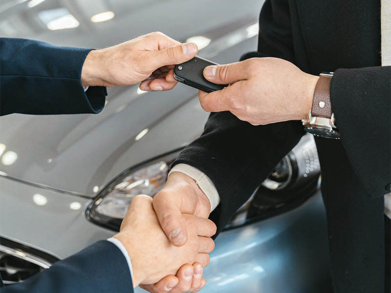 Two people shaking hands while exchanging car keys