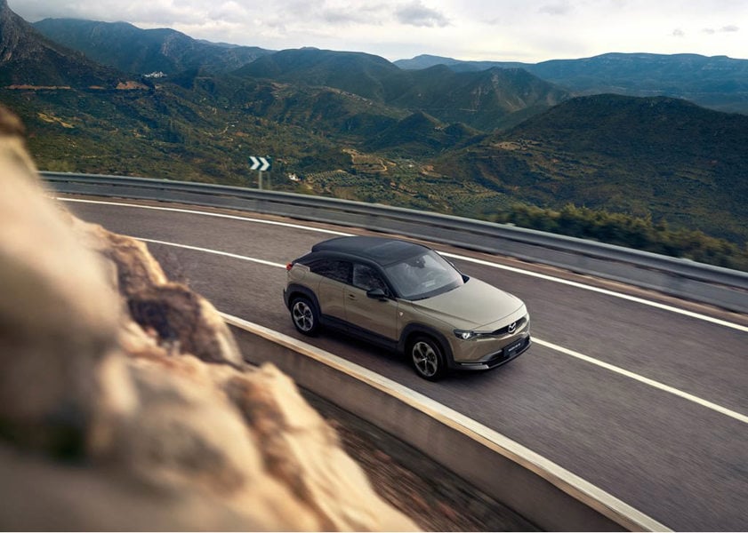 Mazda MX-30 driving on the road with hills in the background