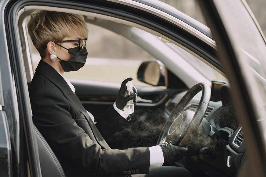 Woman in formal clothes disinfecting steering wheel of car