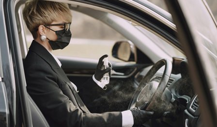 Woman in formal clothes disinfecting steering wheel of car